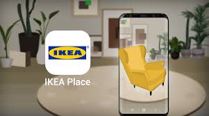 A promotional image for the IKEA Place app, featuring a smartphone displaying an AR view of a yellow armchair placed in a virtual living room setting, surrounded by modern decor and plants.